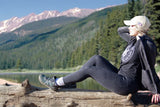 Woman resting on log near mountain lake wearing Xcursion Fusion Spruce style