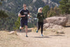 Two people jog along a trail with mountains in the background. Both wear the Aqua X Sport in Surf