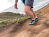 person walking up an inclined trail with shoreline in background, wearing Aqua X Sport in Surf