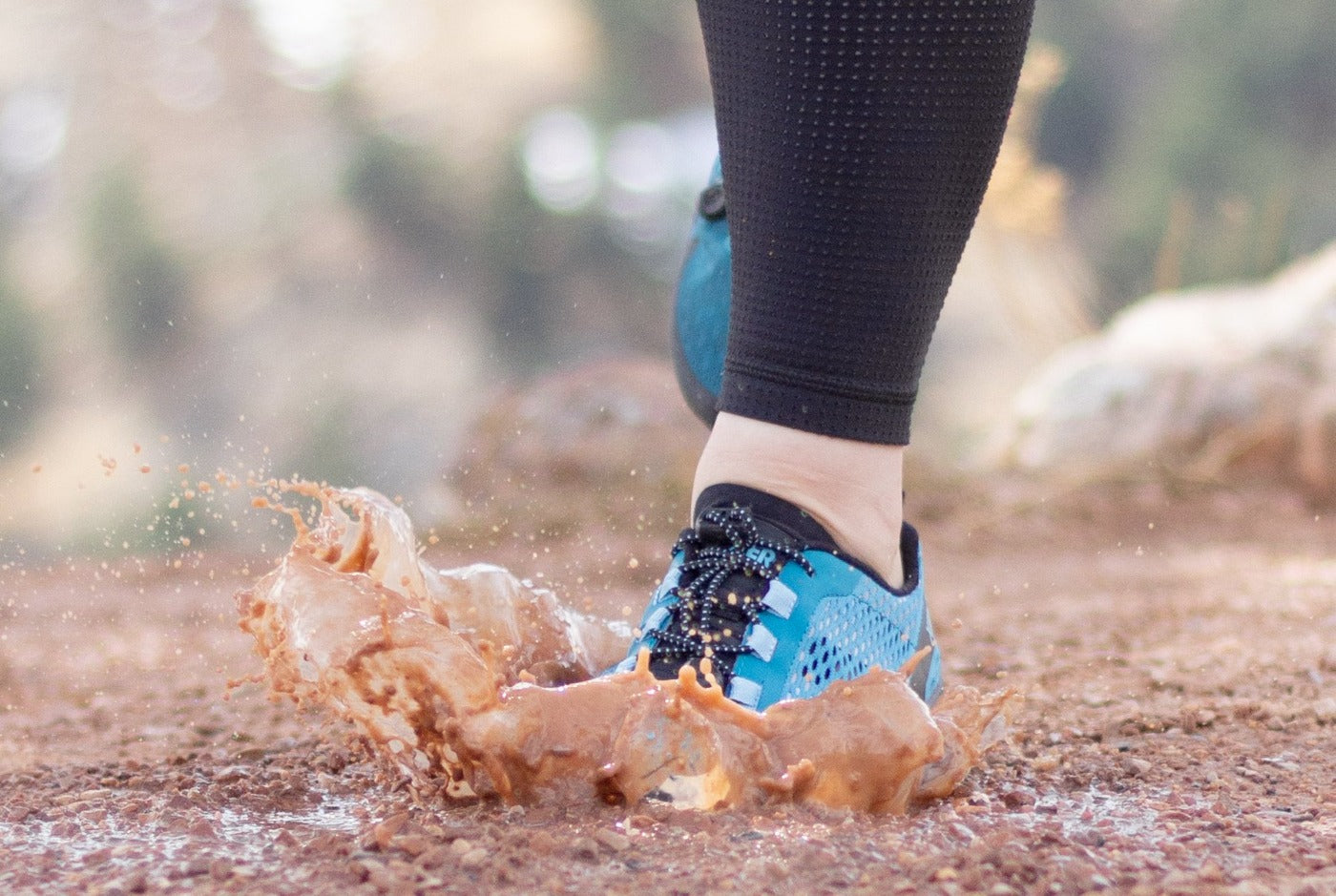 A foot wearing the Aqua X Sport in surf, women's sizing, splashes up mud mid-step