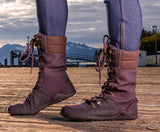 Wearing Mika Chocolate Plum Minimal Womens Boot with jeggings on a wooden dock with mountains in the back