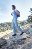 A person walks down a rocky hill in Xcursion Fusion Hikers in blue pants and shirt carrying a full backpack