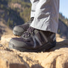 A person stands on a rock top wearing Xcursion Fusion in Bison and light tan hiking pants