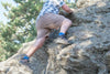 A person climbs up a rocky hill wearing Xcursion Fusion Bison Hikers, Brown Shorts and Blue White plaid shirt