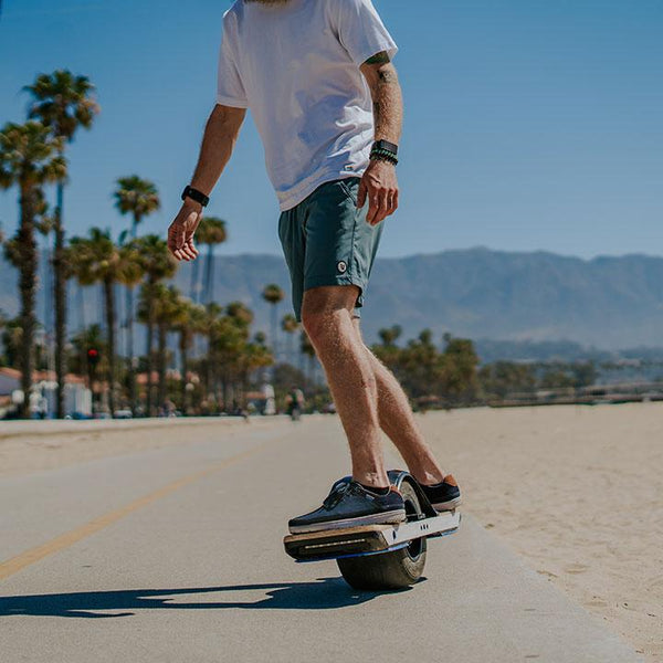 Riding an E-Board at the beach wearing a t-shirt and Lems Chillum Varsity Blue