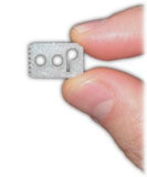 Close-up image of an index finger and a thumb holding the Lace Anchor 2.0. The Lace Anchor 2.0 is a white rectangle about the size of a thumb nail,  with  two holes and a unique p-shaped slot. A zig-zag texture is shown on one edge. White background.